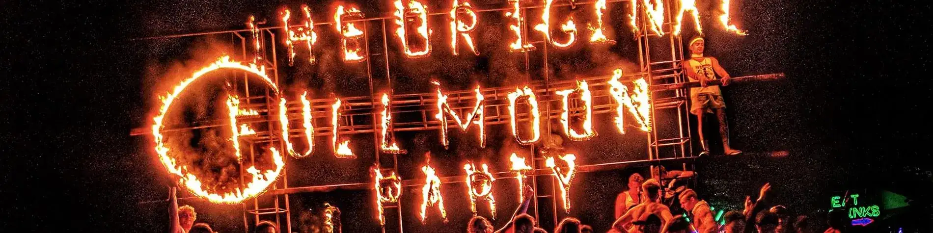 Burning Original Fullmoon Party fire sign with partygoers below at night