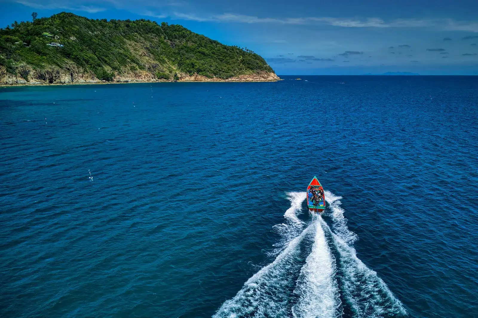Boat leaving a white wake on blue sea near a green Koh Phangan headland