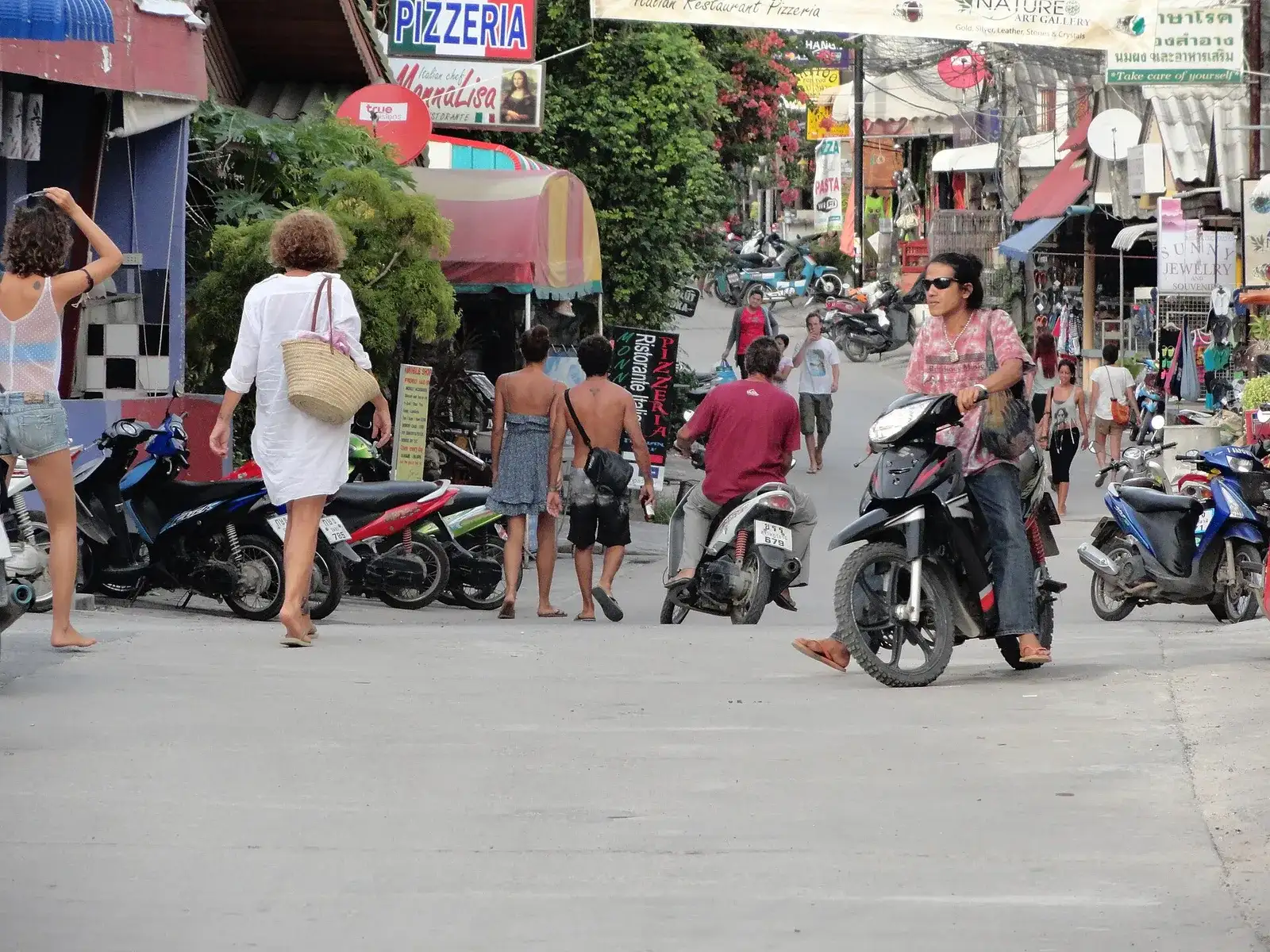 Busy street in Haad Rin village with shops, scooters and walking tourists