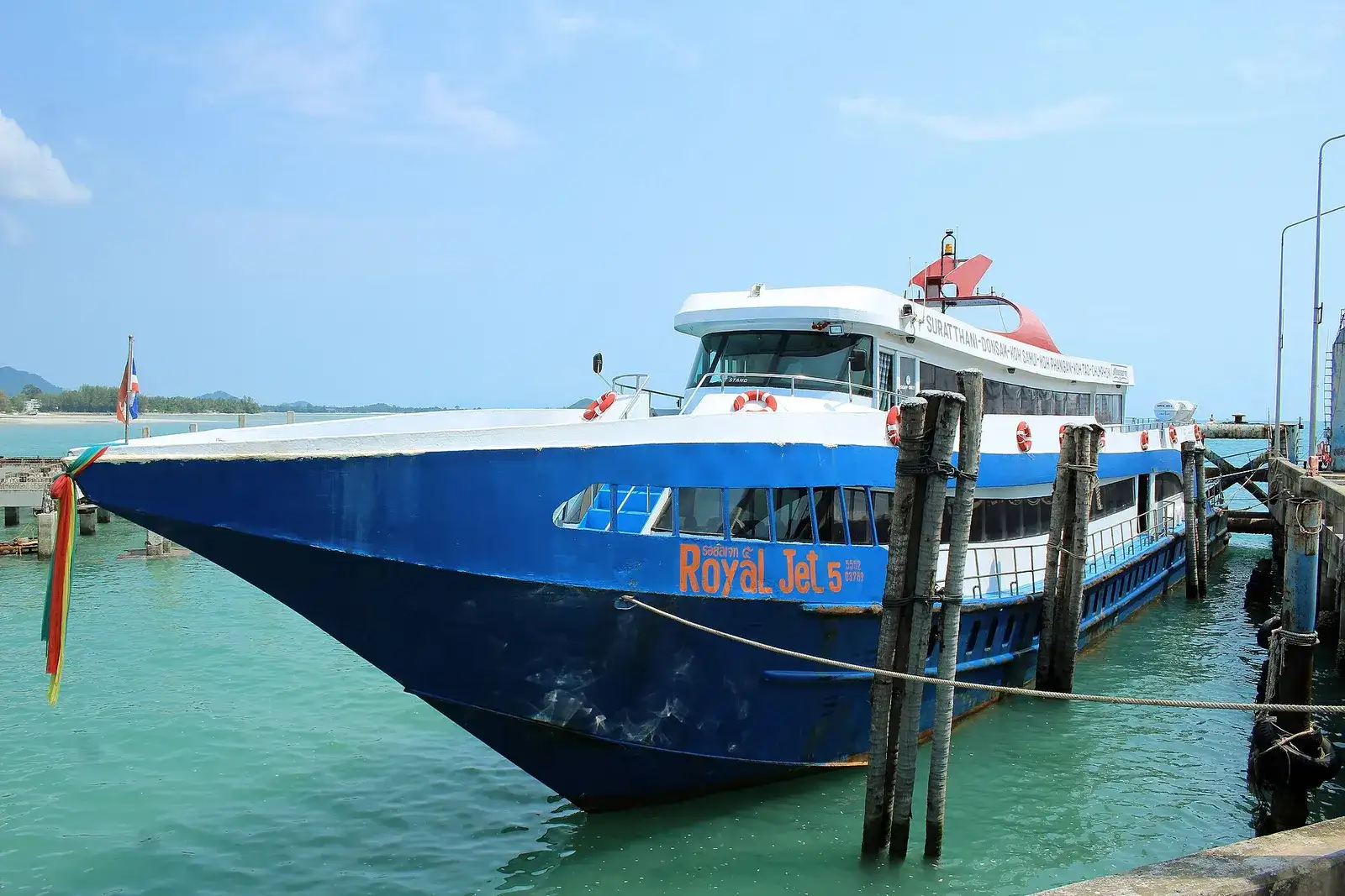 Blue high-speed catamaran ferry moored at a wooden pier in turquoise water