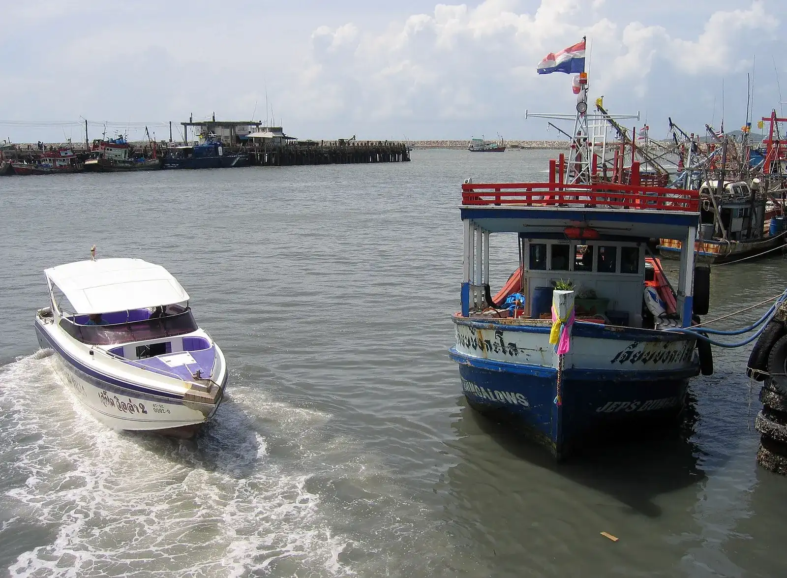 White speedboat pulling away from a busy pier next to a fishing boat